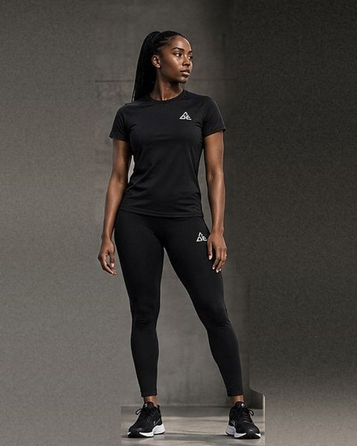 Female model wearing a black GE short-sleeve crew-neck T-shirt and matching ankle-length leggings with white logos.