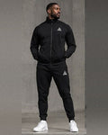 Male model wearing a black GE full-zip stand-collar jacket and matching cuffed joggers with contrasting white GE logos.