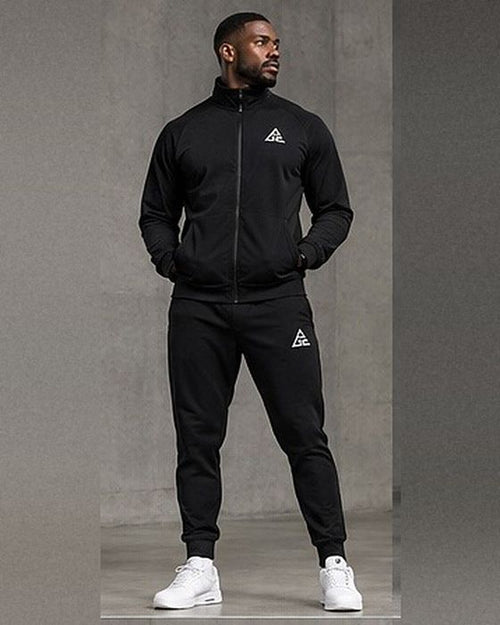 Male model wearing a black GE full-zip stand-collar jacket and matching cuffed joggers with contrasting white GE logos.