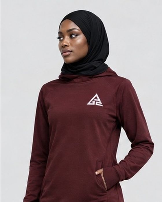 Close-up of the burgundy GE long-sleeve top showing the white chest logo and pocket detail, styled with a black hijab.