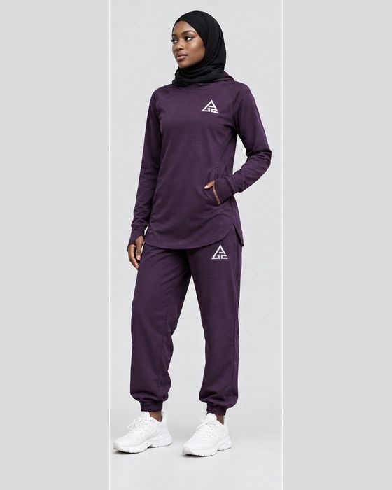 Female model wearing a plum GE longline top and matching cuffed joggers, styled with a black hijab and white trainers.