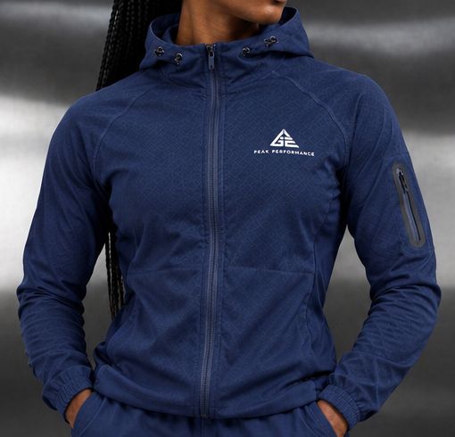 Close-up of the GE navy blue hooded full-zip jacket showing white chest branding and a zipped sleeve pocket.
