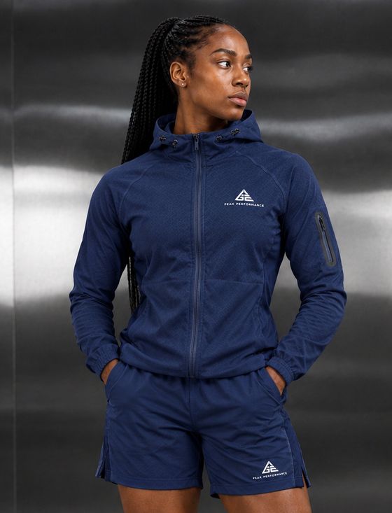 Female model wearing a GE navy blue hooded zip jacket and matching shorts with white GE Peak Performance logos.