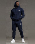 Male model wearing a navy blue GE pullover hoodie with front pouch pocket and matching cuffed joggers with white GE logos.