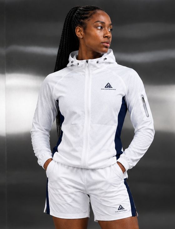 Alternate front view of a female model wearing the GE white hooded jacket and matching blue-panel shorts.