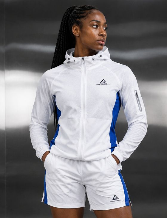 Female model wearing a GE white hooded zip jacket and matching shorts with bright blue side panels.
